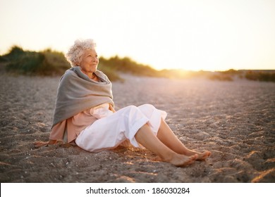 Image of relaxed elderly woman sitting on the beach looking at a view. Senior woman wearing shawl sitting on beach. - Powered by Shutterstock