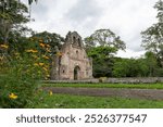 Image of the remains of a colonial-era church in Ujarras, Cartago, Costa Rica. The structure is surrounded by greenery and flowers, with a clear path leading to the entrance