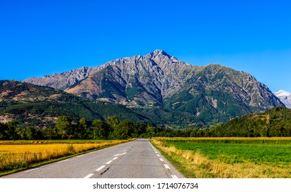 Image of a road going direct to big mountains. It is The Napoleon Road in France leading to Ecrins Massif.