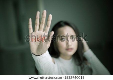Image of sad teenage girl showing help word on her palm while sitting in the dark room