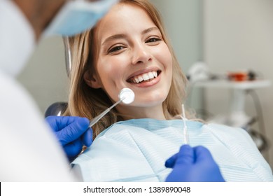 Image of satisfied young woman sitting in dental chair at medical center while professional doctor fixing her teeth - Shutterstock ID 1389890048