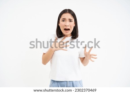 Image of scared asian woman, looking worried and concerned, terrified shouting, standing over white background.