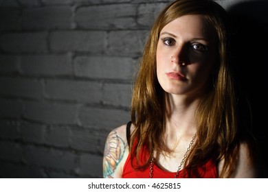 Image Of A Serious Girl With Upper Arm Tattoo.  Harsh Lighting For More Dramatic Effect.