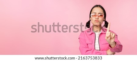 Image of serious, stylish asian girl in sunglasses, showing stop, prohibit gesture, taboo sign, saying no, standing over pink background