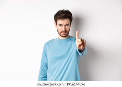 Image of serious young man with beard, shaking finger in disapproval, prohibit or forbid something, standing over white background and saying no - Shutterstock ID 1916144596