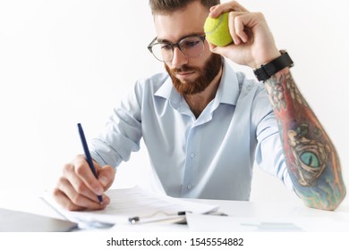 Image of serious young man wearing eyeglasses holding tennis ball while working in office - Powered by Shutterstock