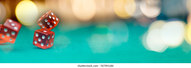 Image of several red dice falling on green table on background of multicolored spots
