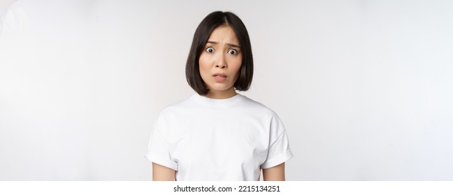 Image of shocked and frustrated asian woman, looking alarmed at camera, cant understand, puzzled, standing over white background. - Shutterstock ID 2215134251