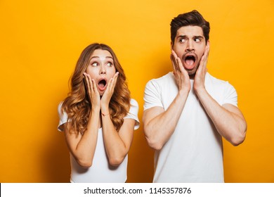 Image of shocked people man and woman in basic clothing expressing surprise or fright with open mouth covering face isolated over yellow background