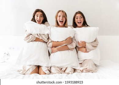 Image Of A Shocked Young Girls Women Friends Indoors On Bed At The Hen Party At Home Holding Pillows.