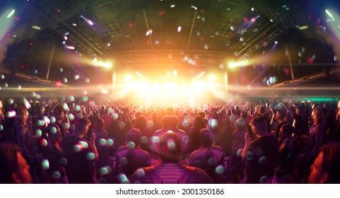 Image shot during a music festival. Light comes from a stage with a band show, people silhouettes are visible in front of it. - Shutterstock ID 2001350186