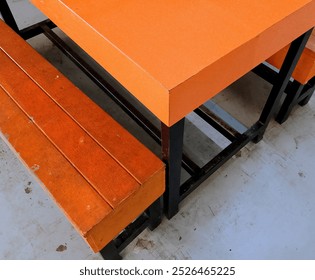 The image showcases a simple yet sturdy outdoor dining set, composed of an orange wooden bench and a matching table with a metal frame - Powered by Shutterstock