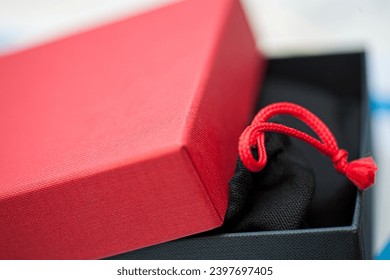 The image showcases a striking red gift box with its lid slightly ajar, revealing a peek of a black velvet pouch secured with a vibrant red drawstring. The bold contrast between the box's vivid hue