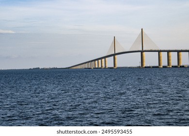 Image showcasing a long, modern cable-stayed bridge spanning over a vast body of water. The bridge features tall pylons and multiple support columns, stretching across the horizon.