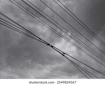 An image showcasing overhead power lines set against a backdrop of dark, stormy clouds, depicting a moody and dramatic sky.  - Powered by Shutterstock