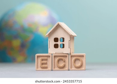 An image showcasing a small wooden house model placed on wooden blocks spelling ECO, with a blurred globe in the background, symbolizing eco-friendly housing or living - Powered by Shutterstock