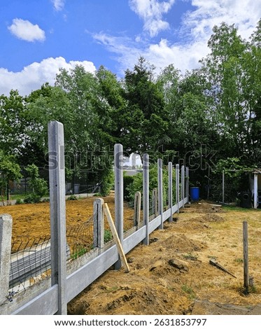 Image showing the construction of fence between neighboring properties. Image showing a boundary line fence being built in a residential area. Concrete and wood modern fence assembly on property line.