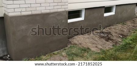 Image showing a fresh newly applied cement parging of an exterior house foundation wall, chimney, and around two windows with a clean work area - Quebec Canada.