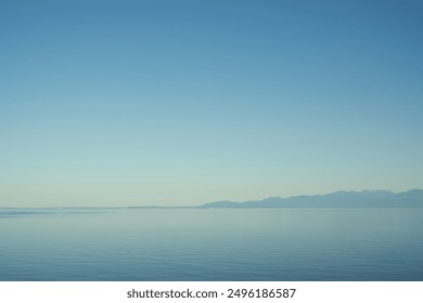 The image shows a calm sea under a clear blue sky with distant mountains on the horizon, creating a serene and peaceful scene. - Powered by Shutterstock