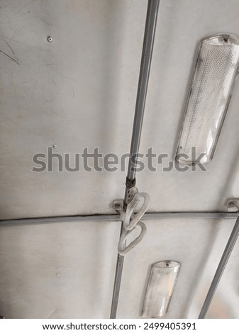 The image shows the ceiling of a bus with hanging straps and overhead lights. The ceiling is white and the straps are grey.