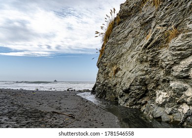The image shows a cliff extending down to the black sand beach on the coast of California