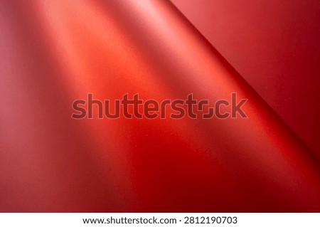 The image shows a close-up, abstract view of flowing red fabric. The fabric has a smooth, satiny texture with dramatic lighting that creates highlights and shadows.