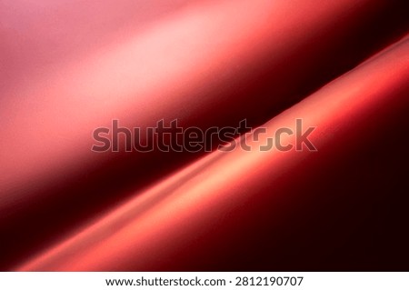 The image shows a close-up, abstract view of flowing red fabric. The fabric has a smooth, satiny texture with dramatic lighting that creates highlights and shadows.