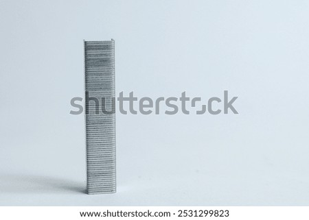 The image shows a close-up of a stack of metallic staples placed on a clean white surface. The staples are organized neatly, showing their straight, parallel lines.