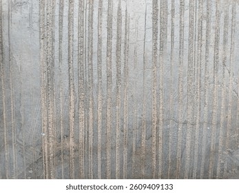 The image shows a close-up of a surface with vertical textured lines. The background appears to be a grayish, weathered concrete or stone surface
