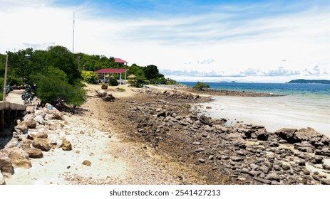 The image shows a coastal scene with a rocky shore, trees, buildings, and a clear sky. - Powered by Shutterstock