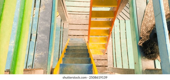 The image shows a colorful wooden staircase leading up to a platform. The stairs are painted in bright shades of yellow, blue, and green. The platform is made of wooden planks and has  railing .       - Powered by Shutterstock