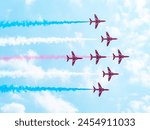 The image shows a formation of nine fighter jets flying in a diamond pattern against a backdrop of a clear blue sky with some scattered clouds. The jets are colored in a combination of red, white, and