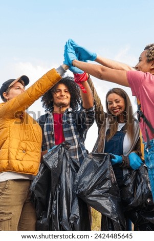 The image shows a group of enthusiastic volunteers celebrating their successful environmental cleanup. The team, consisting of a diverse mix of individuals, is seen raising gloved hands together in a