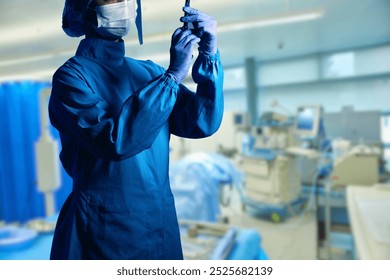 The image shows a healthcare professional, fully dressed in surgical scrubs, gloves, and a face mask, preparing or adjusting a syringe in a clinical or surgical setting.  - Powered by Shutterstock