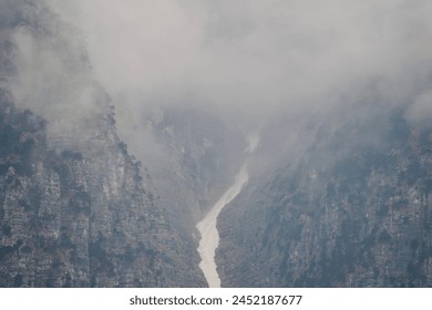 
The image shows a misty mountain gorge with a narrow snow-filled crevice between steep, rugged cliffs, creating an ethereal and mystic atmosphere. - Powered by Shutterstock