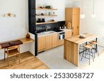 The image shows a modern kitchen with light wood cabinets, open shelves, and a workspace. It features a built-in oven, black backsplash, and a central island with stools, creating a clean atmosphere.