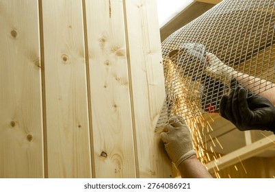 The image shows a person using an angle grinder to cut or shape a piece of expanded metal mesh near a wooden structure.