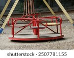 The image shows a red, round, metal merry-go-round playground equipment with handrails and seats. It is designed for children to sit or stand on while spinning around.