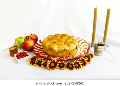 The image shows a Rosh Hashanah setting with round challah, apples, honey, pomegranate seeds, flowers, two candles, and a silver cup, symbolizing sweetness and blessings for the Jewish New Year. - Powered by Shutterstock