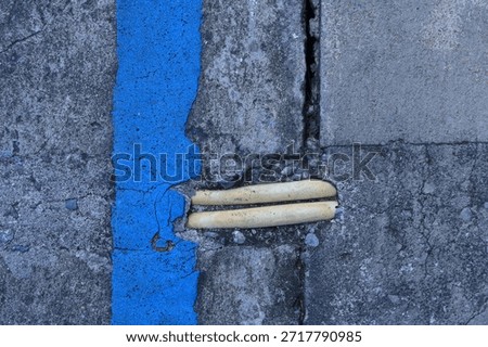 The image shows section of two exposed yellow underground electrical PVC conduits, embedded within cracked gray rough concrete pavement. The conduits have become exposed due to damage to the surrounding concrete surface.