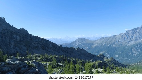 The image shows a serene mountain valley with snow-capped peaks, lush green trees, and a clear blue sky. - Powered by Shutterstock