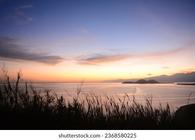 The image shows a serene sunset over a vast body of water, with a small island in the distance. The sky is painted with vibrant colors, creating a stunning backdrop for the scene. - Powered by Shutterstock