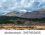 The image shows a snowy mountain in the distance in the Scottish Highlands. It captures the natural beauty of the outdoor landscape with snow-covered peaks and trees.