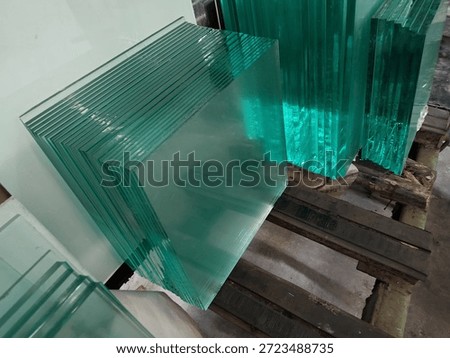The image shows a stack of several thick glass panes standing vertically in an industrial or warehouse setting.