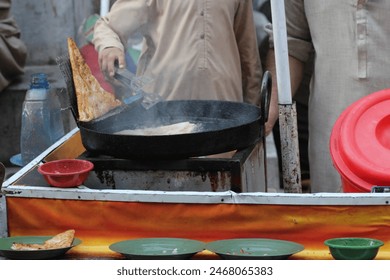 image shows a street food vendor frying food in a large pan the vendor is likely preparing a popular snack or dish setting appears to be an outdoor market or food stall - Powered by Shutterstock