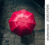 The image shows a top-down view of a person holding a vibrant red umbrella while standing on a wet pavement.