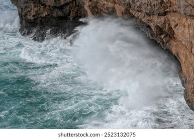 The image shows turbulent sea waves crashing against a rugged cliff, creating a dynamic and powerful display of nature’s force. The scene captures the raw energy and beauty of the ocean in motion. - Powered by Shutterstock