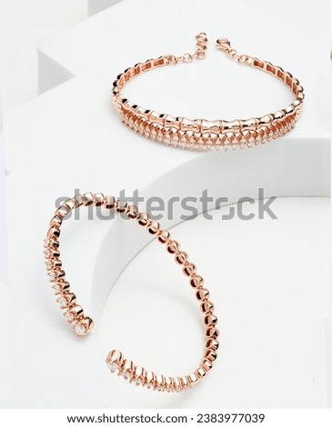 
The image shows two gold bangles with diamonds. The bangles are made of yellow gold and have a simple, rounded design. Each bangle is encrusted with small diamonds, which gives t