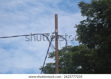 The image shows a utility pole, likely a metal or rust-coated steel one, with several cables and wires attached to it. The pole appears to be supporting communication or power cables