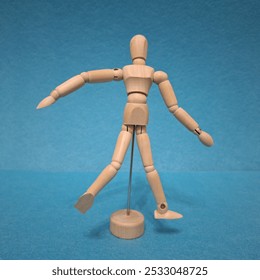 The image shows a wooden artist's mannequin in a walking pose. The figure has movable joints that allow for adjusting its posture, and it is standing on a small circular base supported by a metal rod. - Powered by Shutterstock